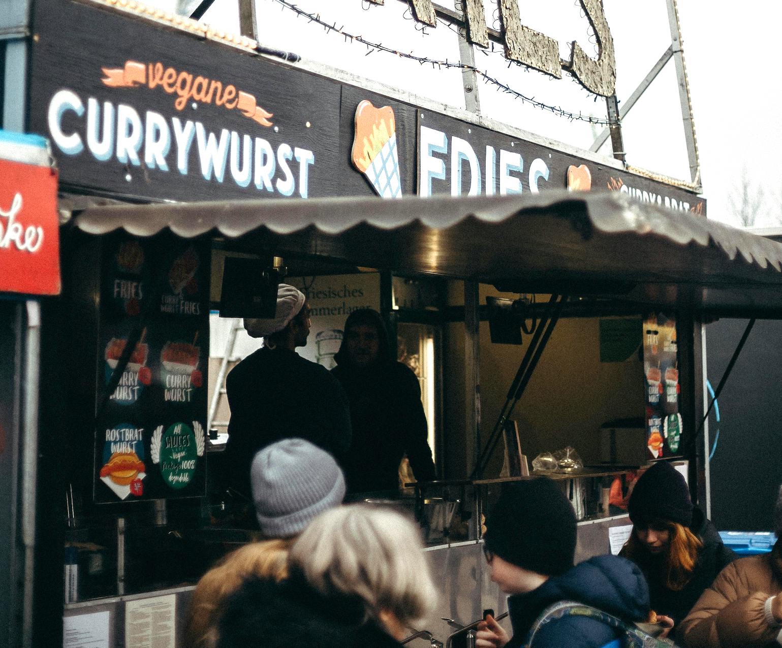 A Berlin outdoor street food stall offering fries and vegan Currywurst at a market, showcasing the city’s evolving food culture and plant-based options.