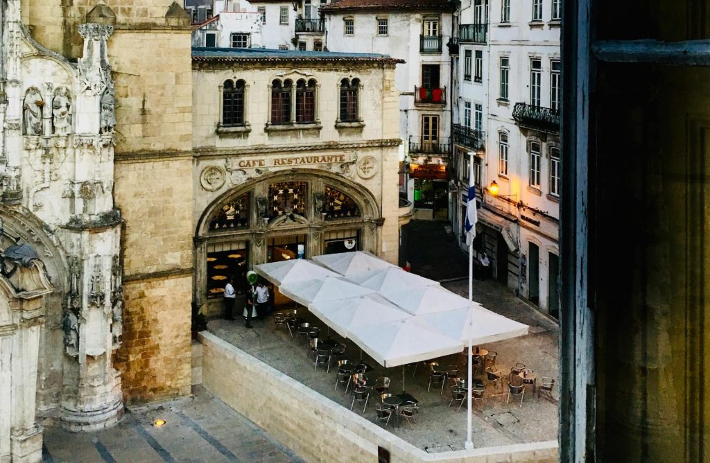 People enjoying traditional Portuguese cuisine at Café Santa Cruz in Coimbra, Portugal, seated at outdoor tables in a historic setting.