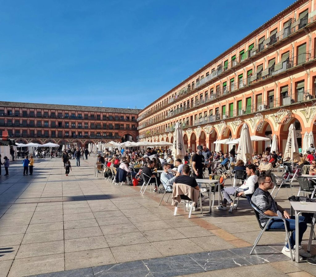 People enjoying meals at outdoor restaurants near a traditional building in Córdoba, Andalusia, Spain, reflecting the social dining culture.