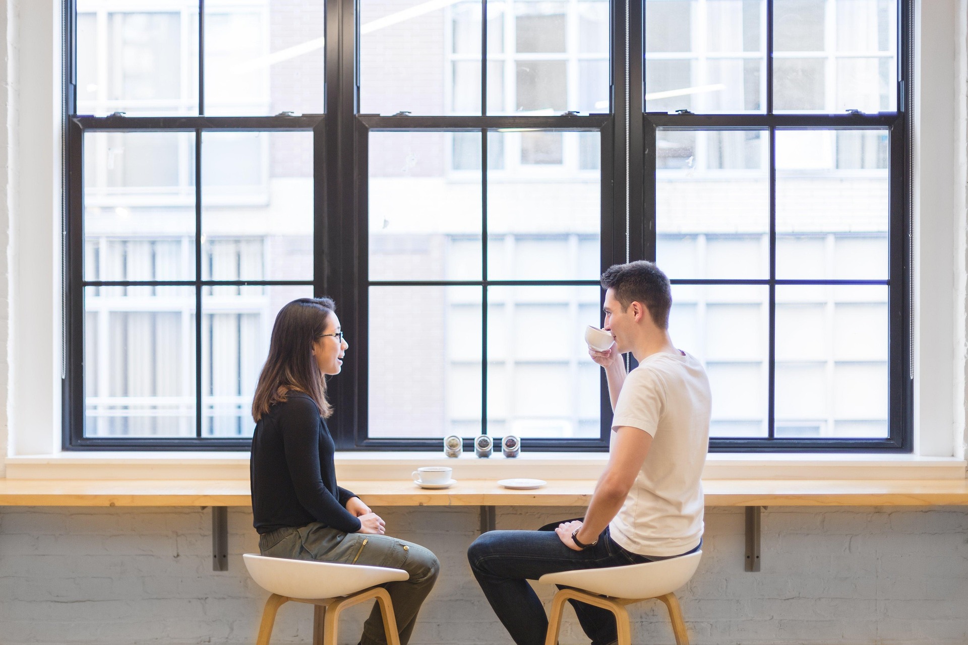 A man and a woman sitting by a window, sipping coffee while talking, symbolizing tenants discussing rental issues and finding solutions for an unresponsive landlord.