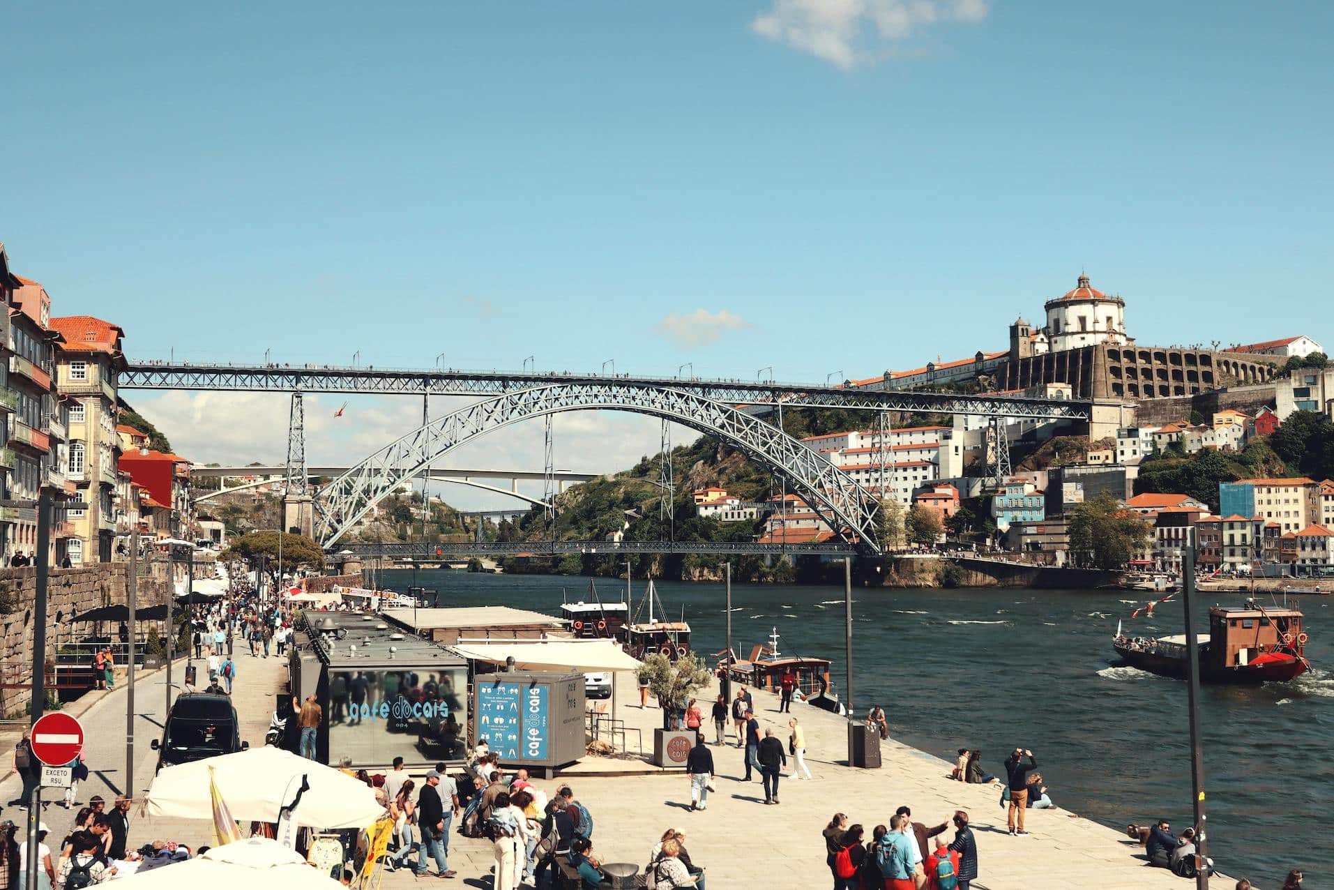 People enjoying a sunny day near the Dom Luís I Bridge in Porto, Portugal, reflecting the country’s emphasis on community and work-life balance.