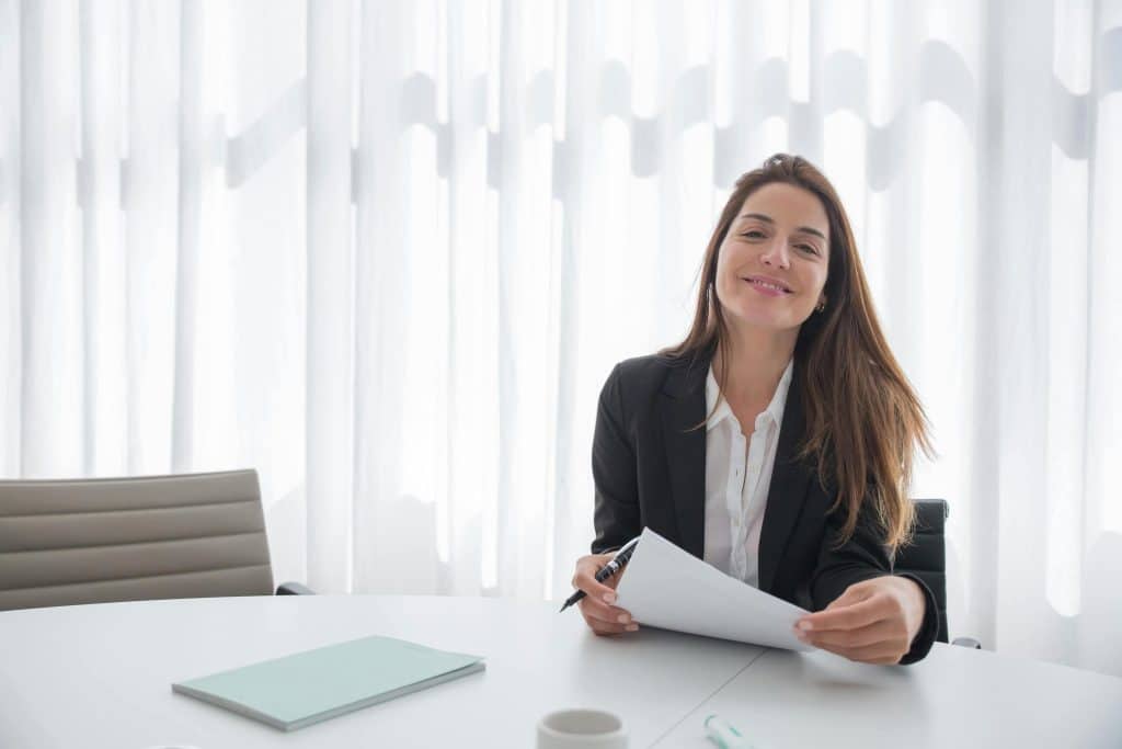 Woman smiling in a professional setting while holding paperwork, representing preparation for the Portugal work visa application process.