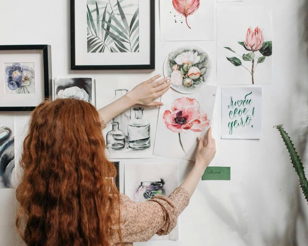 A woman putting a paper with a drawing on the wall, showcasing a renter-friendly way to personalize a space without permanent changes.