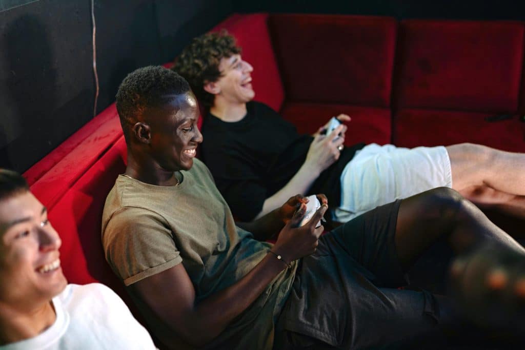Three friends of diverse backgrounds laughing and playing video games in their shared apartment, enjoying life in a co-living space.