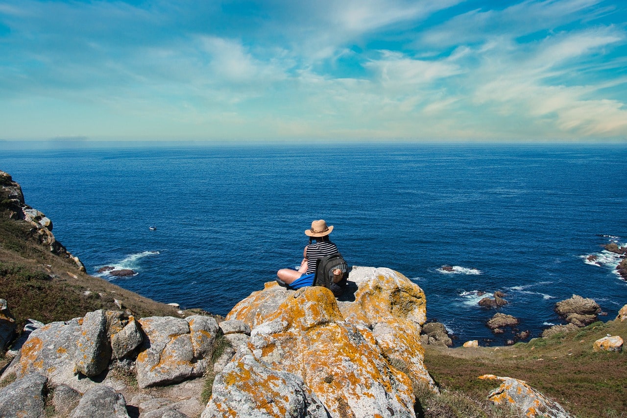 A girl sitting on a cliff, gazing at the ocean in Spain, showcasing the country's stunning coastal landscapes.