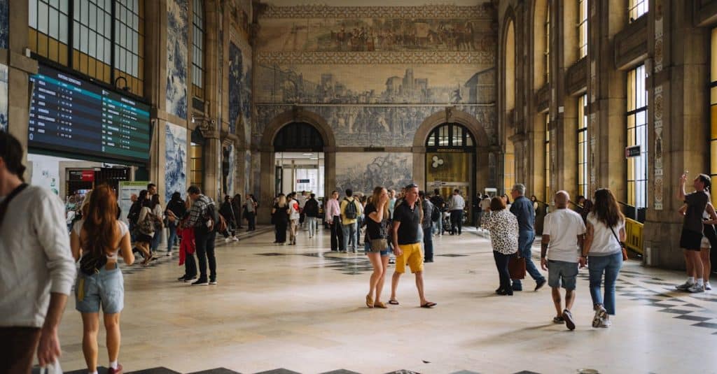 Gothic architecture of São Bento train station in Porto, Portugal, with tourists and locals exploring the grand hall adorned with traditional azulejo tiles.