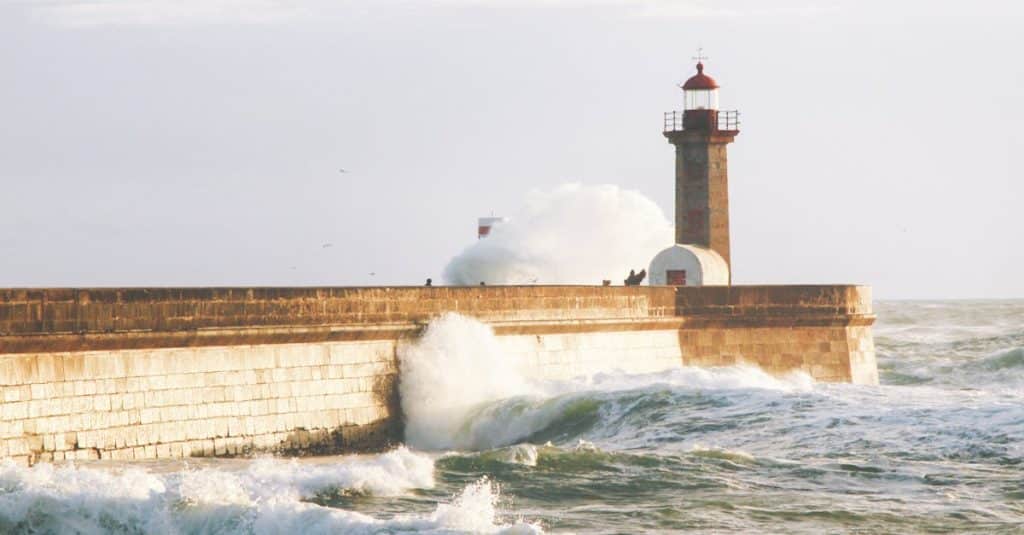 Scenic view of crashing waves against the Douro River lighthouse in Porto, Portugal, showcasing the dramatic coastal beauty of Foz do Douro.