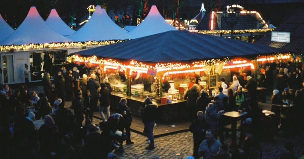 Colorful and bustling Christmas market in Berlin, Germany, showcasing festive lights and a lively crowd at night, celebrating the holiday season.