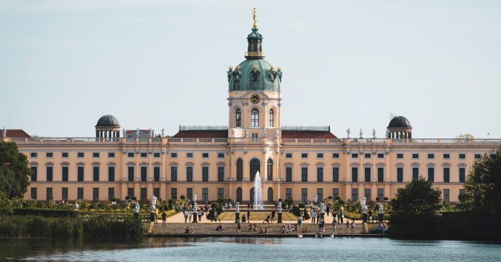 Stunning view of Charlottenburg Palace with a serene lake and a vibrant summer scene in Berlin, Germany, showcasing the district’s historical and luxurious charm.