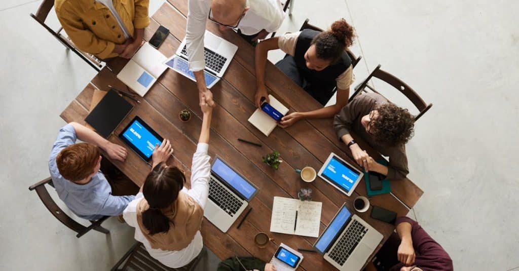 A diverse team collaborating in an office in Spain, using laptops and tablets, showcasing cooperation and work culture for expats.