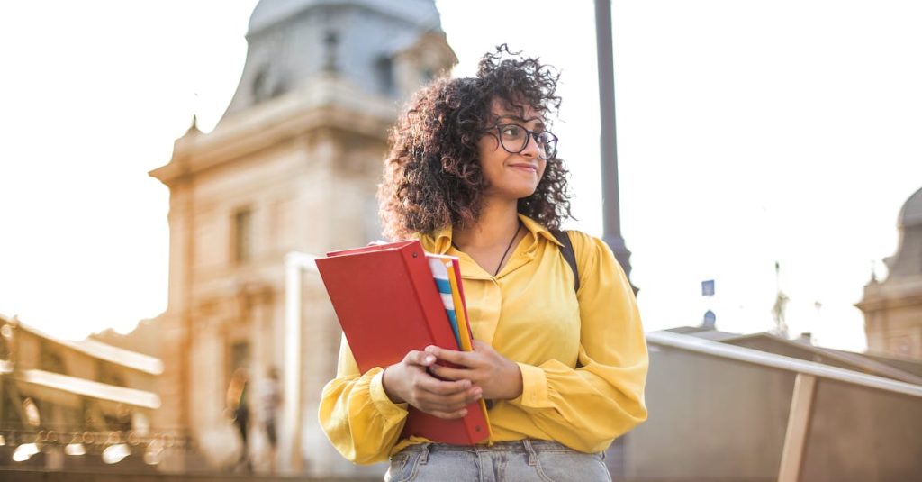 Smiling female student holding books on campus steps at a French university.