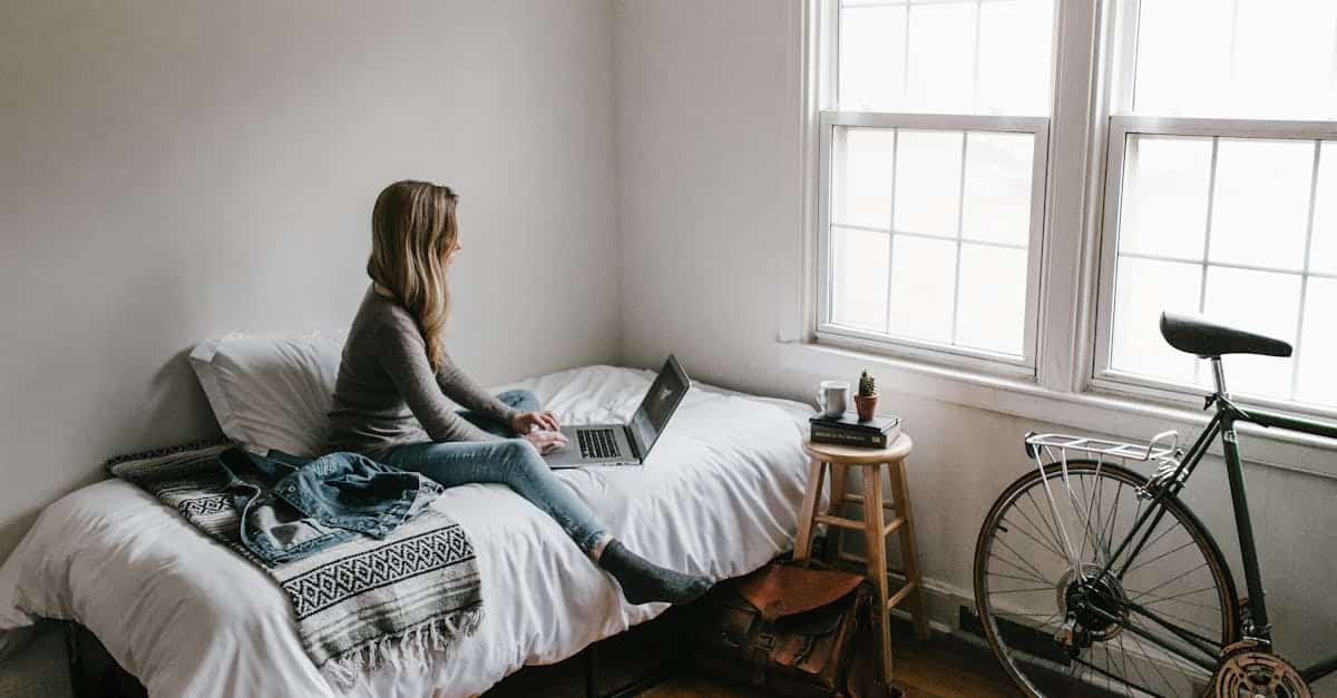 A young woman works on a laptop in a cozy, minimalist bedroom setting, showcasing the remote learning lifestyle for German language learners.