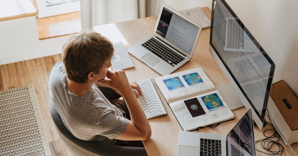 Top view of a young programmer working on multiple laptops in a modern office setting, representing Berlin’s thriving freelance and remote work culture.
