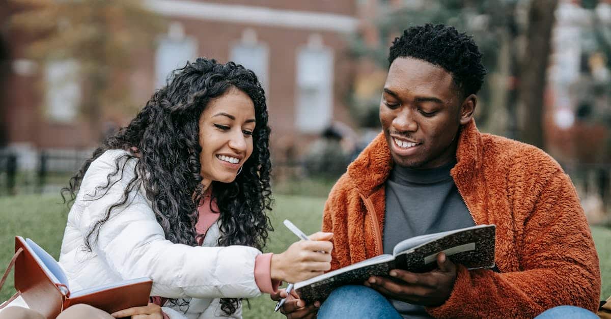Happy college students studying together on a campus lawn, sharing ideas and writing notes, reflecting the vibrant student life in Portugal.