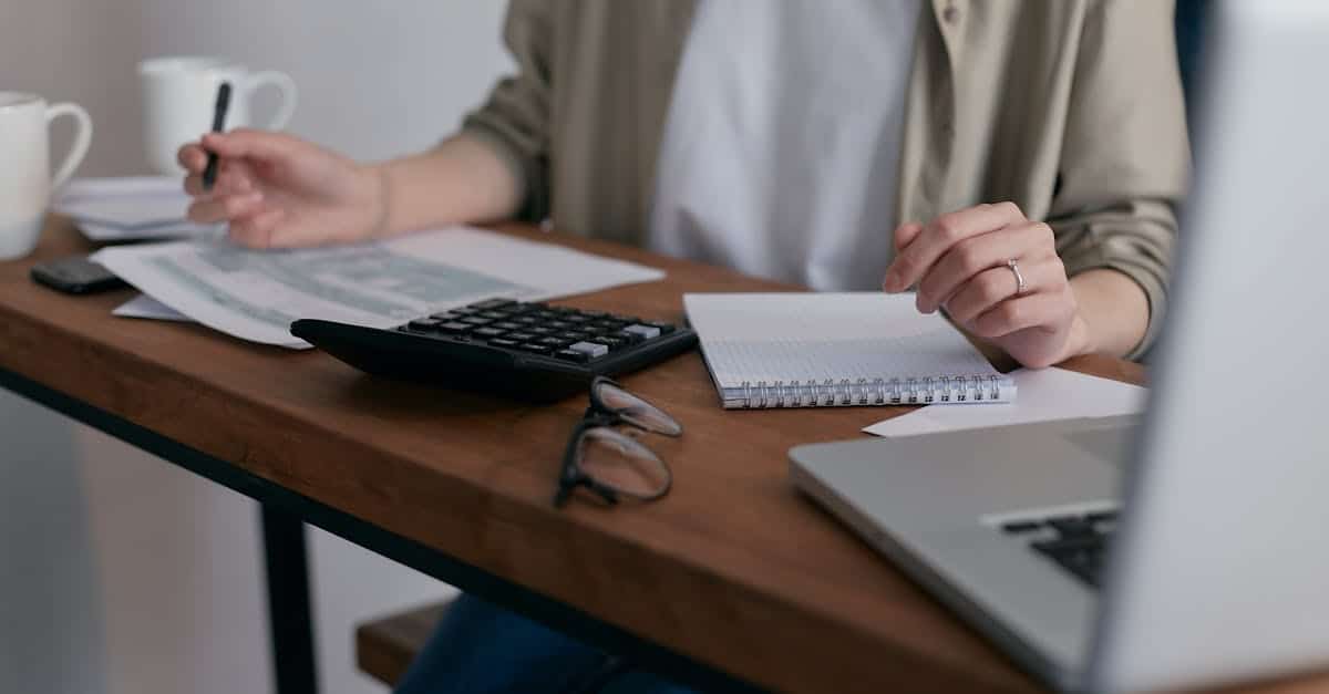 A woman managing finances at home, using a laptop and calculator on a wooden desk, representing tax planning for expats in Berlin.