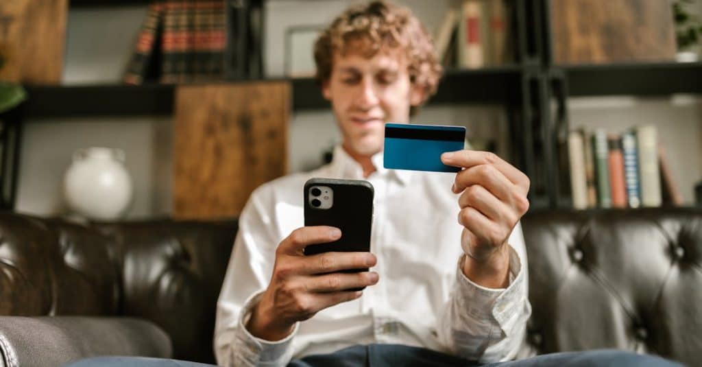 Man using a smartphone and credit card for an online money transfer, highlighting digital banking options in Portugal.