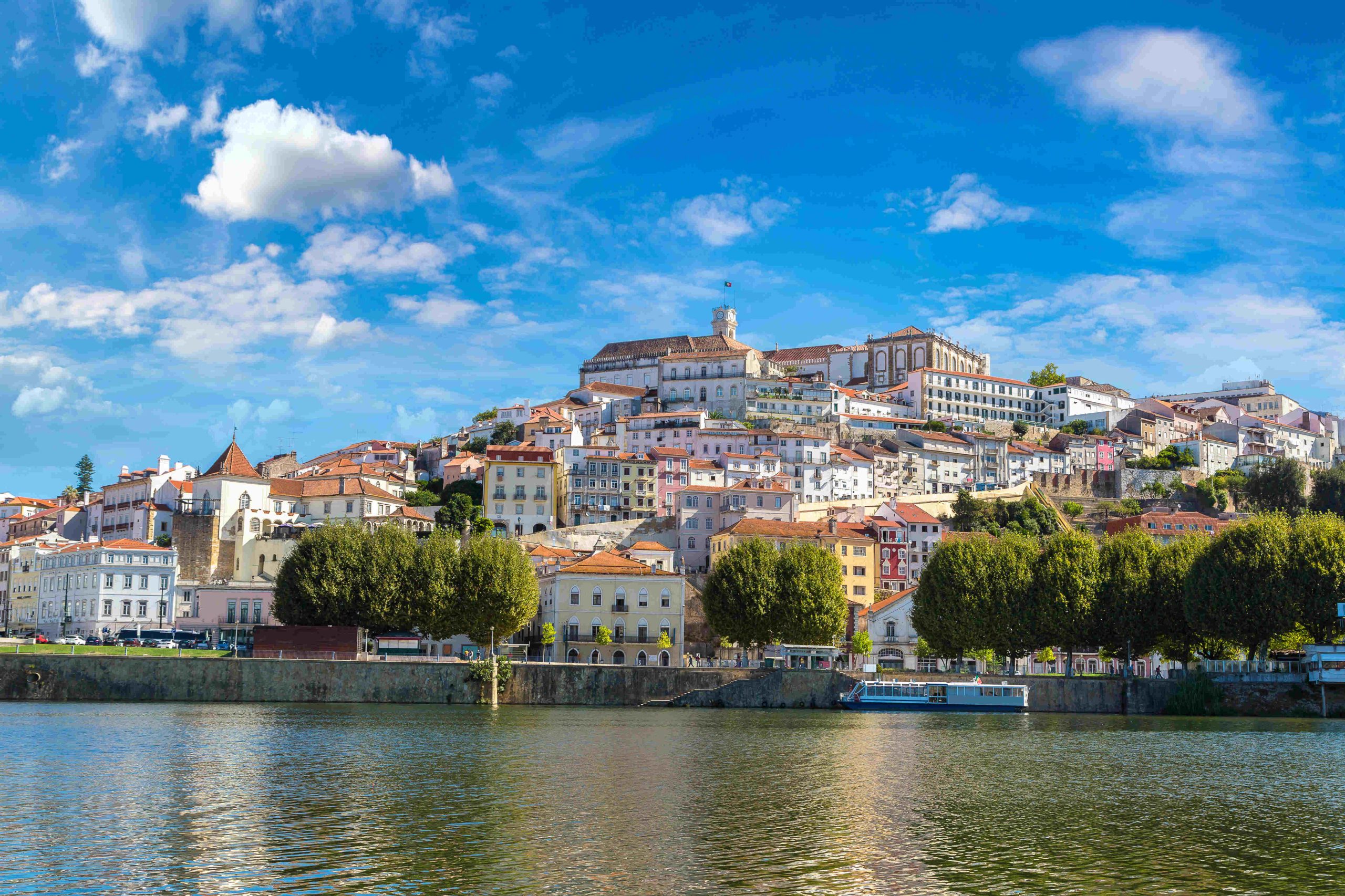 Panoramic city view of Coimbra, Portugal, featuring the historic university, Mondego River, and traditional houses on the hillside.