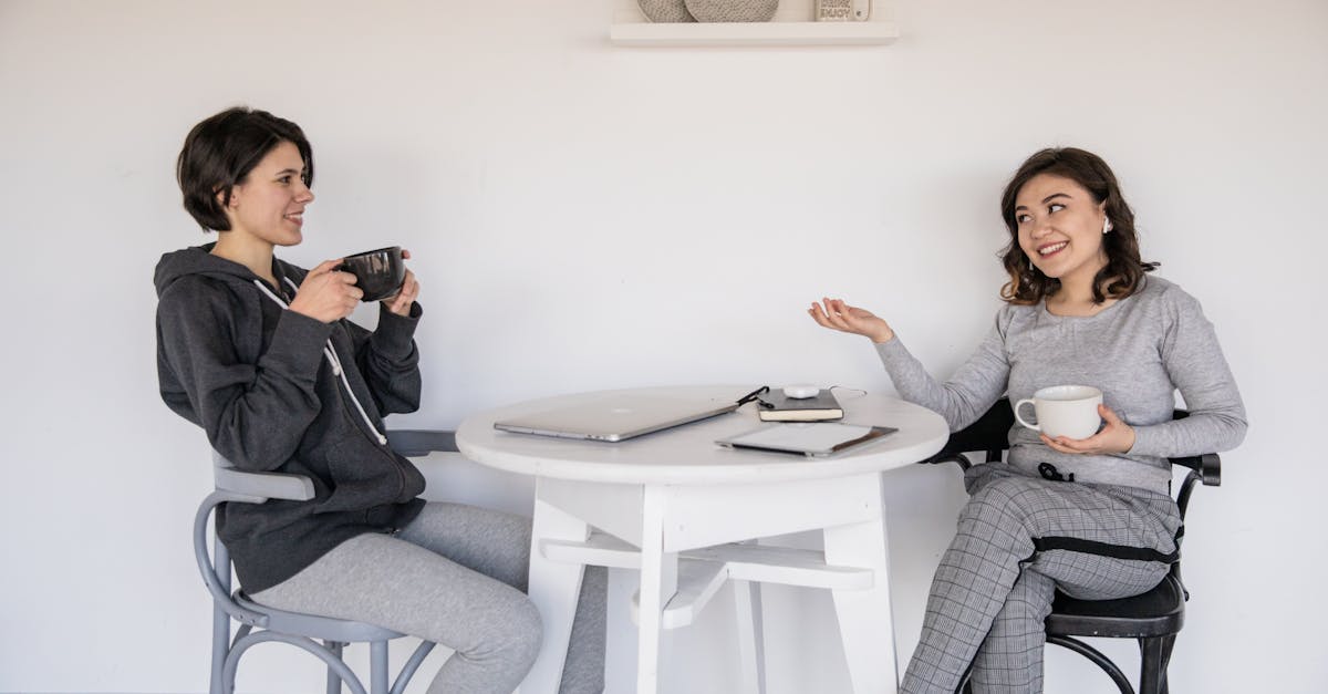 "Two women enjoying a friendly chat over coffee indoors, smiling and engaging in open communication while respecting different social styles.