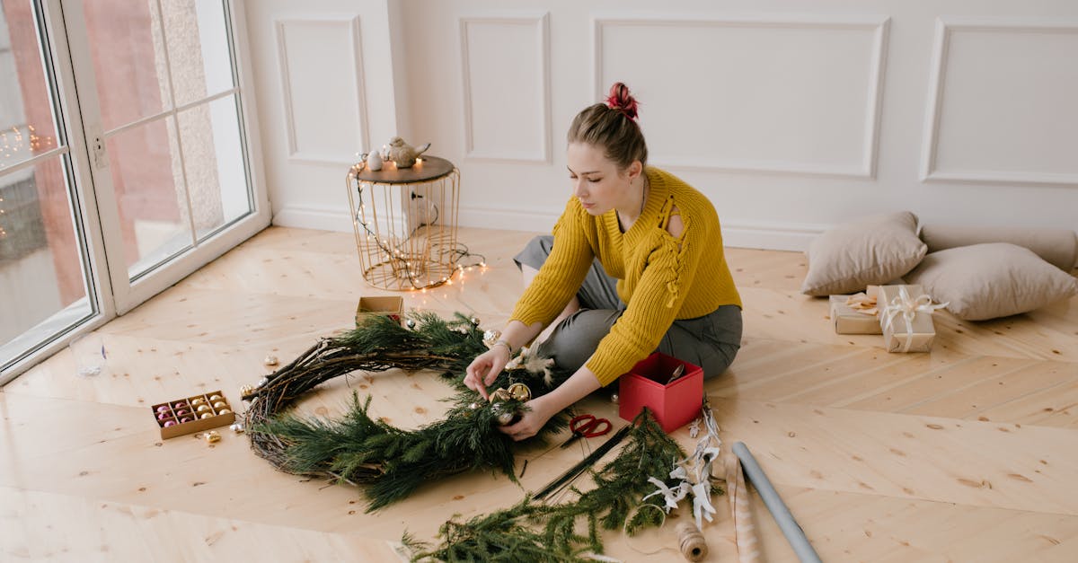 A young woman in a cozy room crafting a festive Christmas wreath by the window, showcasing budget-friendly DIY holiday decor ideas.
