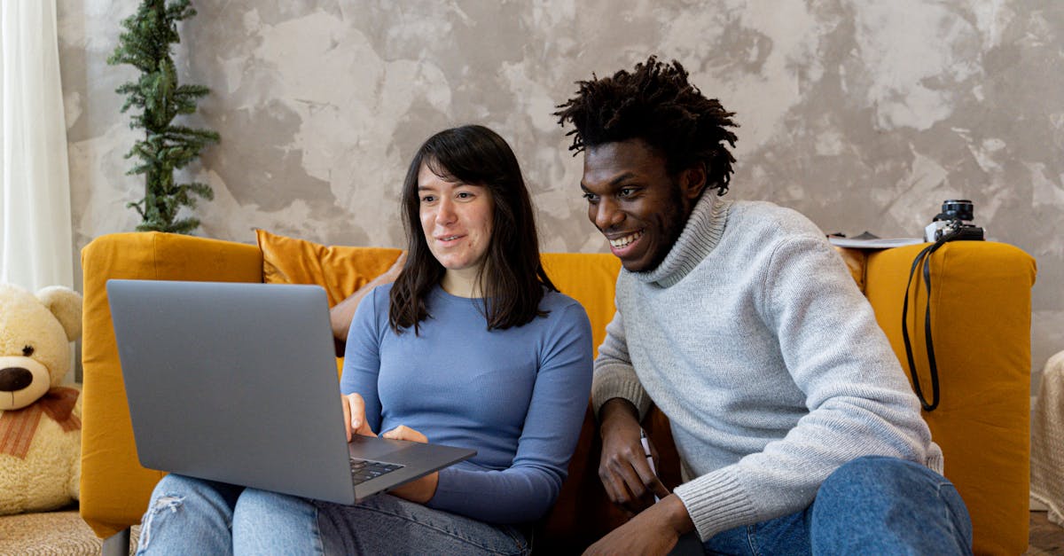 Two friends sitting on a cozy couch, smiling while looking at a laptop, managing shared utility expenses in their apartment.