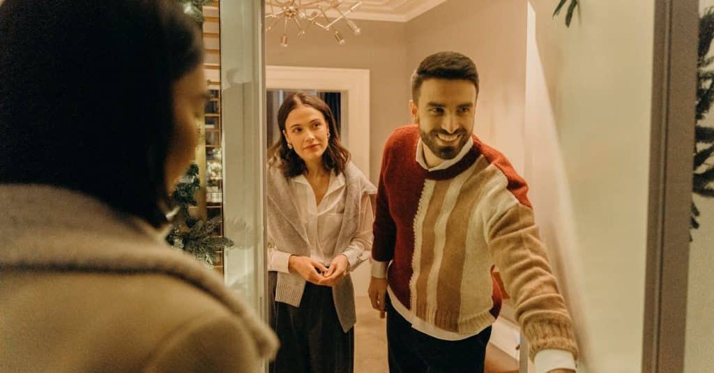 A couple greeting a guest at their doorway, creating a warm and welcoming atmosphere for an overnight stay in a shared living space.