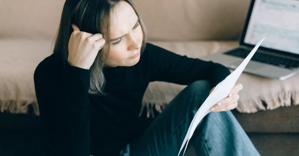 A focused woman analyzing papers with a laptop open, symbolizing thoughtful consideration while reviewing a rental contract.