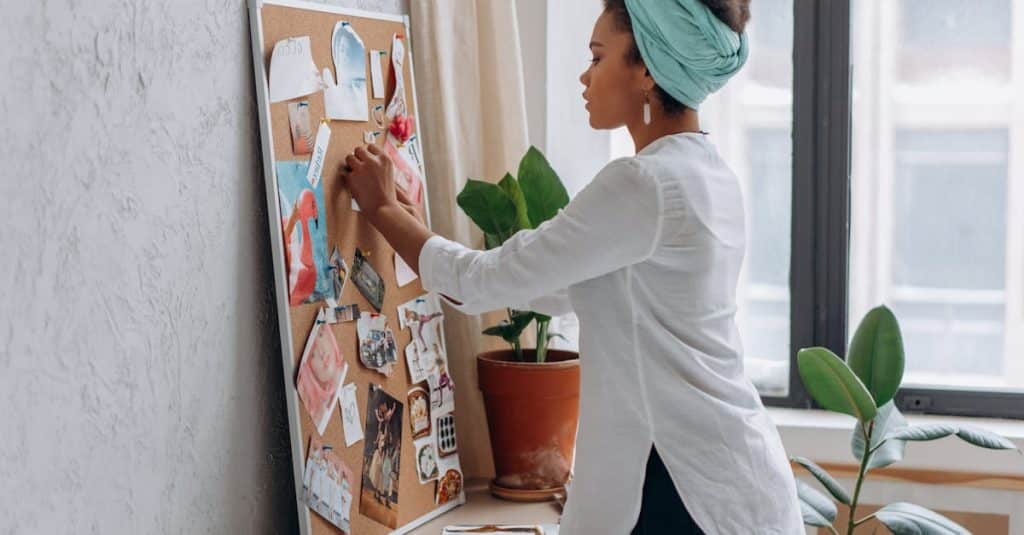 A woman in a white shirt arranging a vision board in a modern apartment with plants nearby, showcasing renter-friendly plant decor ideas.