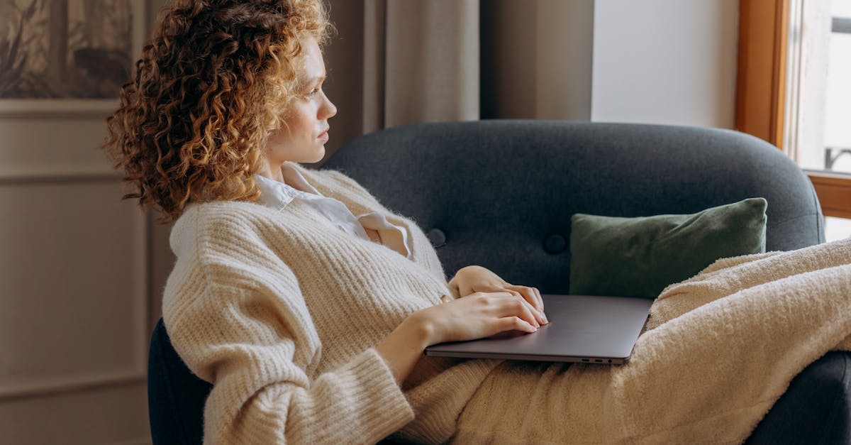 A woman with curly hair lounges on a sofa, holding a laptop and enjoying a peaceful moment in her shared apartment, maintaining personal space and roommate boundaries.