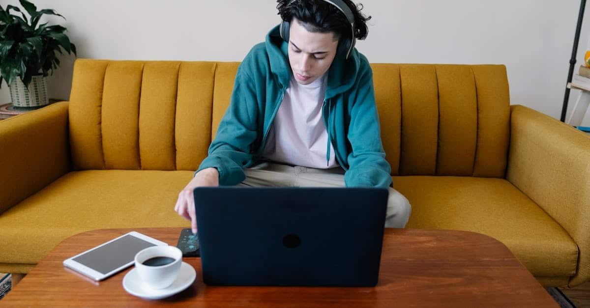 A busy young male in headphones sitting on a sofa and using a cellphone at a table with a netbook, coffee, and tablet, illustrating ways to manage noisy neighbors in a rental home.