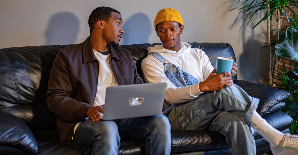 Two men engaged in discussion on a couch with a laptop and coffee mug, fostering effective communication in a shared living space.