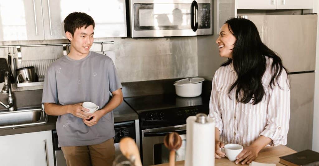 Happy friends chatting over coffee in a bright, modern kitchen, discussing meal planning and shared grocery shopping.