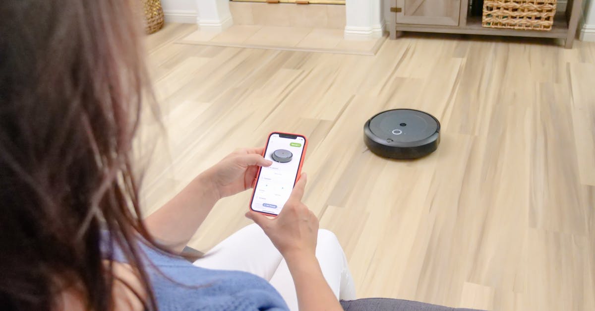 Overhead view of a woman controlling a robot vacuum using a smartphone app on a wooden floor, showcasing DIY smart home upgrades for renters.