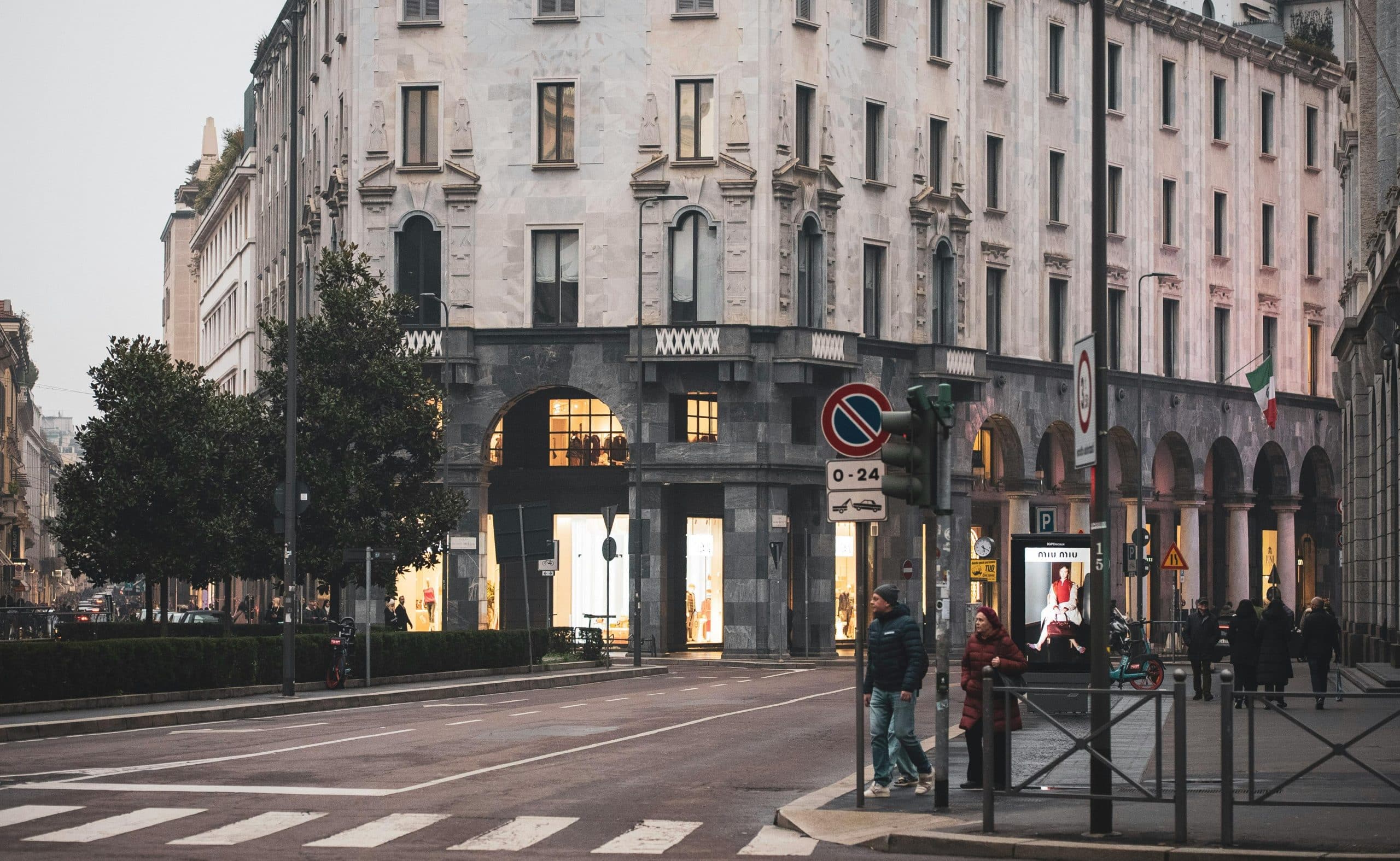 Street view showcasing historic architecture in Milan, Italy with pedestrians and traffic lights.