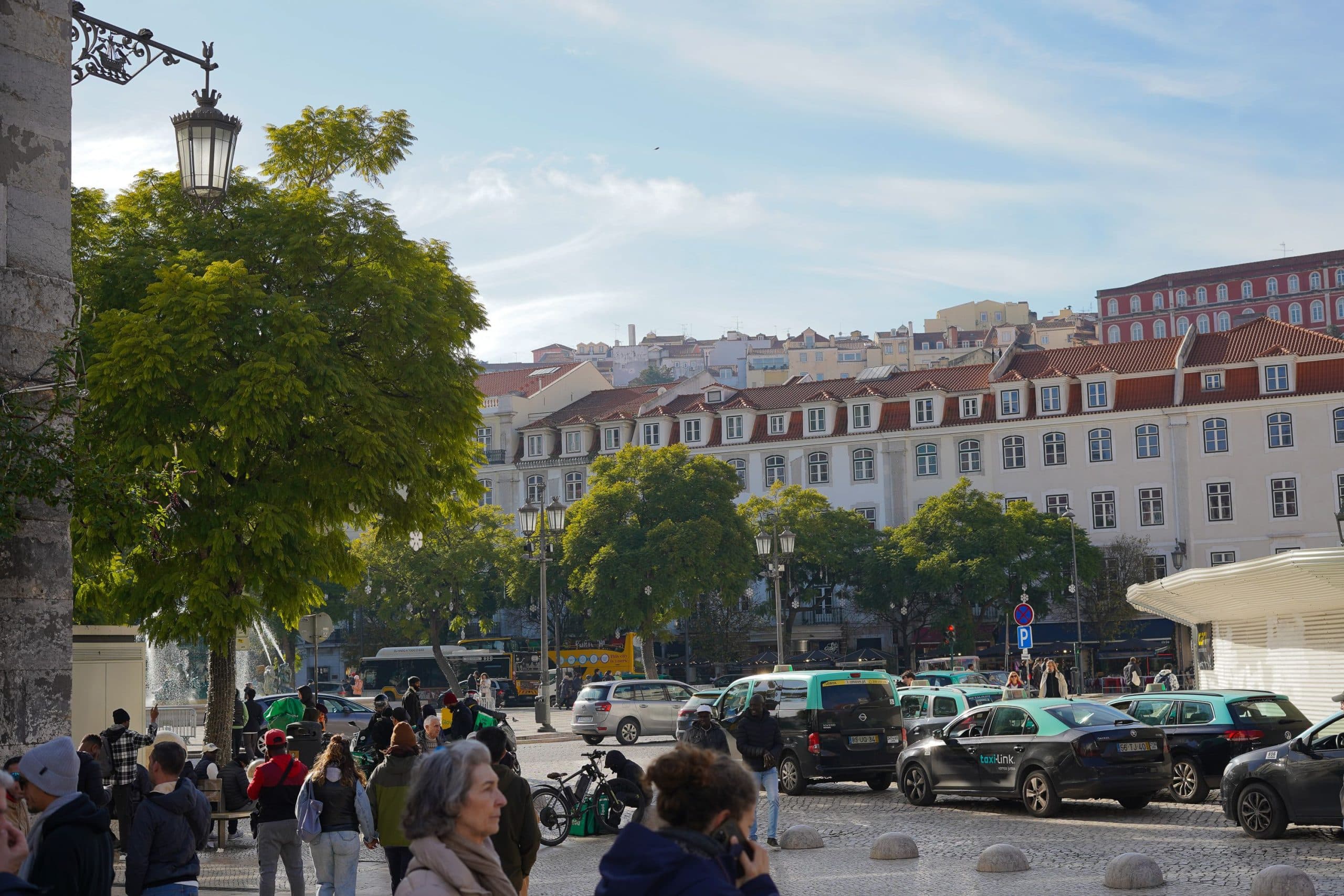 Lively daytime view of a bustling street in Lisbon with classic European architecture and people.