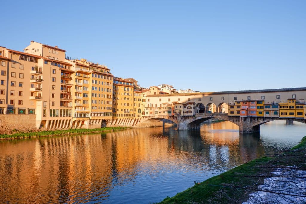 Beautiful sunset view of Ponte Vecchio reflected on the Arno River in Florence, Italy.